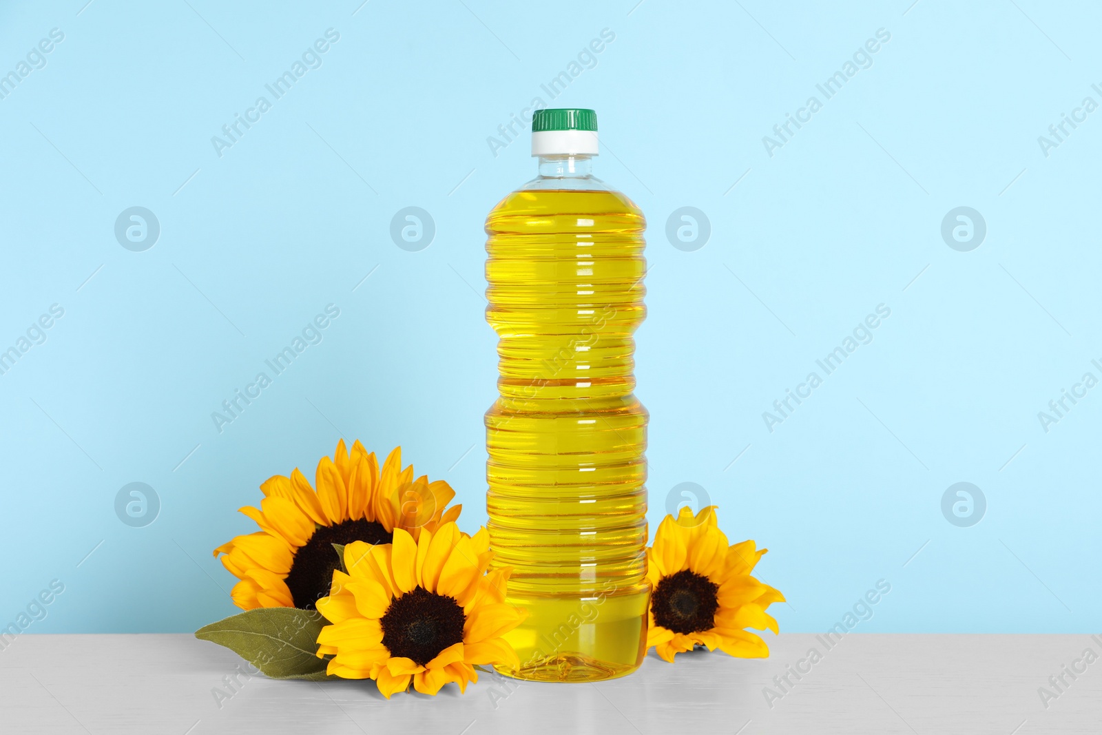 Photo of Bottle of cooking oil and sunflowers on white table