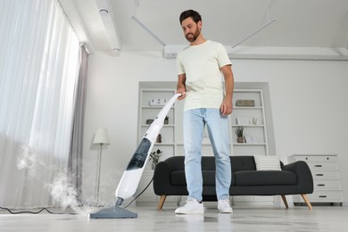 Photo of Happy man cleaning floor with steam mop at home, low angle view