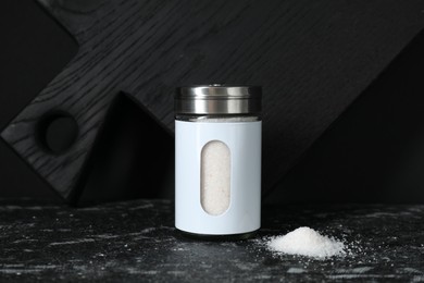Stylish shaker with salt on dark table