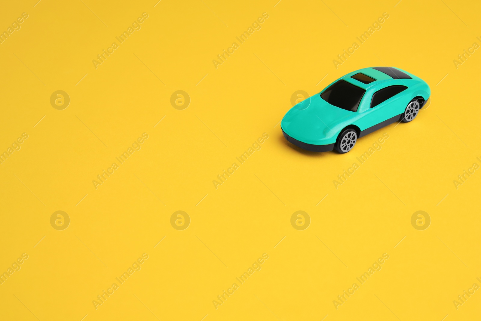 Photo of One turquoise car on yellow background, space for text. Children`s toy