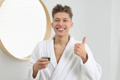 Photo of Young man with mouthwash showing thumbs up in bathroom