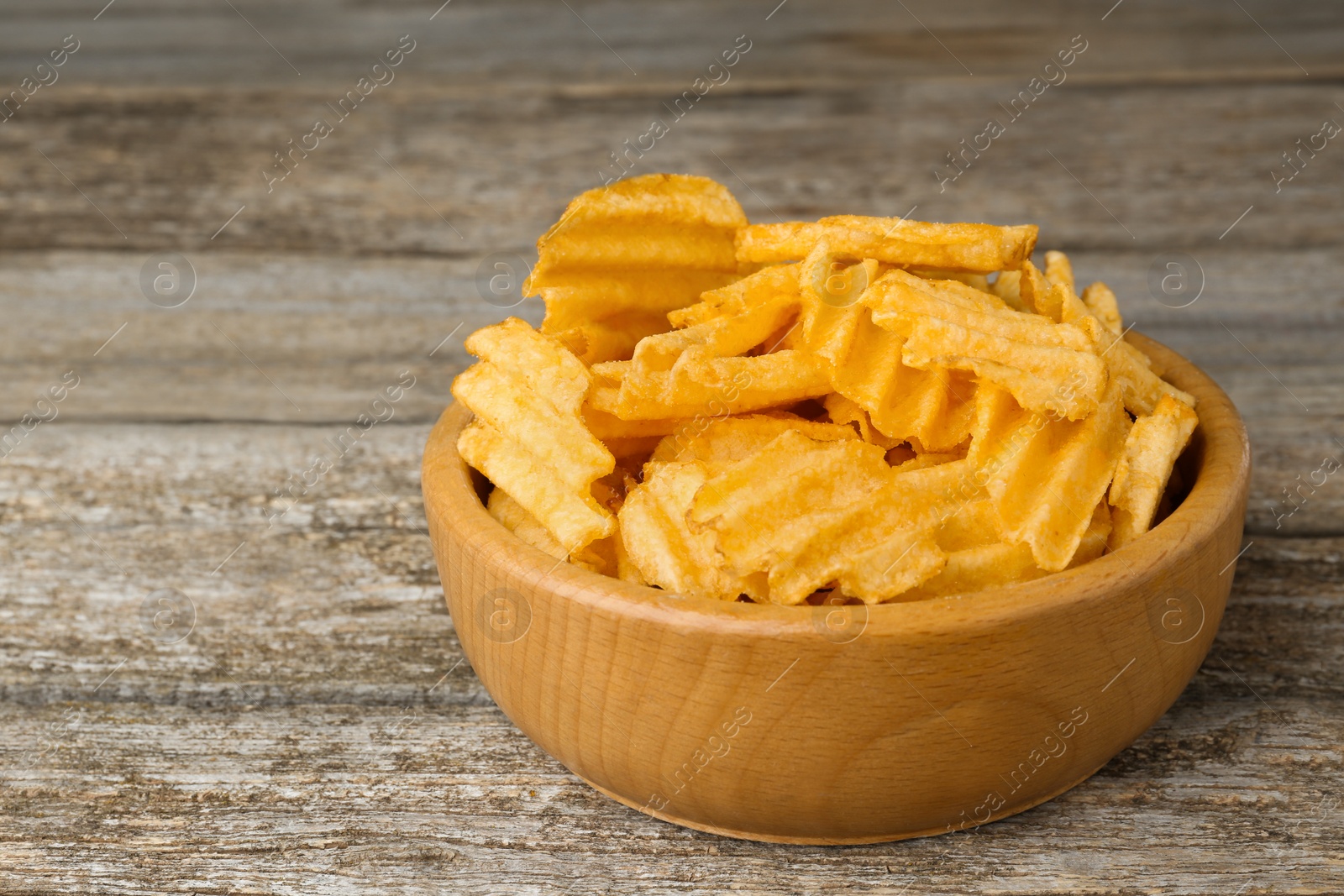 Photo of Bowl with delicious ridged potato chips on wooden table, closeup. Space for text