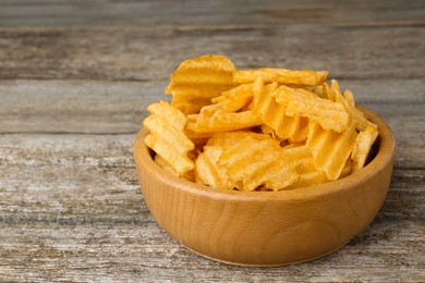 Bowl with delicious ridged potato chips on wooden table, closeup. Space for text