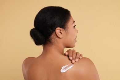 Photo of Young woman applying body cream onto back on beige background