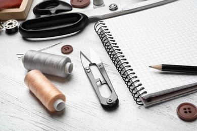 Bobbins with threads, scissors and notebook on table. Tailoring accessories