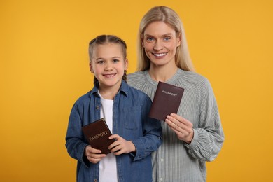 Photo of Immigration. Happy woman and her daughter with passports on orange background