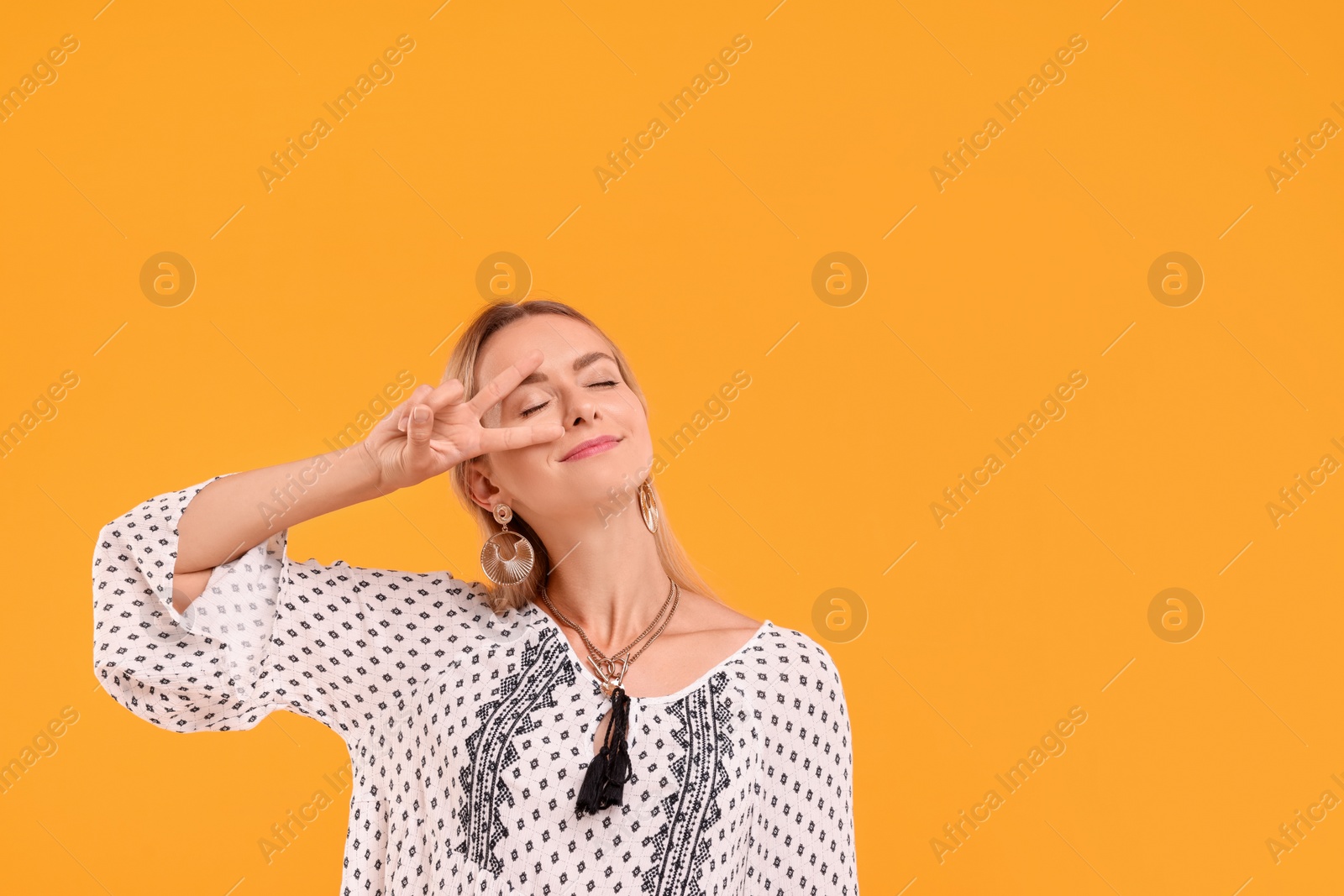 Photo of Portrait of hippie woman showing peace sign on yellow background. Space for text