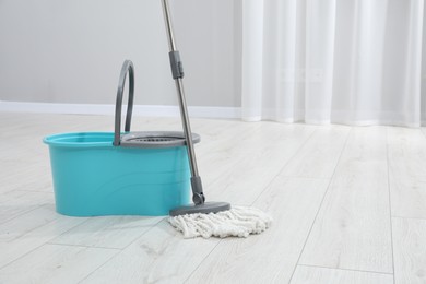 Photo of Mop and plastic bucket indoors. Space for text