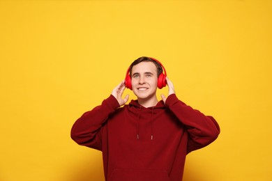 Handsome young man with headphones on yellow background