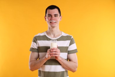 Photo of Happy man with milk mustache holding glass of tasty dairy drink on orange background