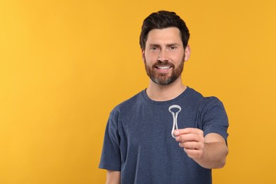 Happy man with tongue cleaner on yellow background, space for text