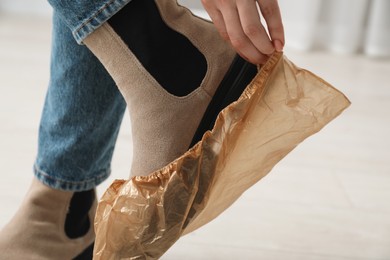 Photo of Woman wearing shoe cover onto her boot indoors, closeup