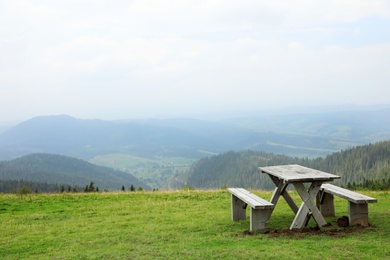 Photo of Picturesque landscape with wooden picnic table and mountain forest on background