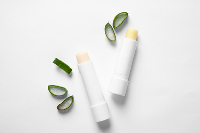 Photo of Hygienic lipsticks and cut aloe vera leaf on white background, top view