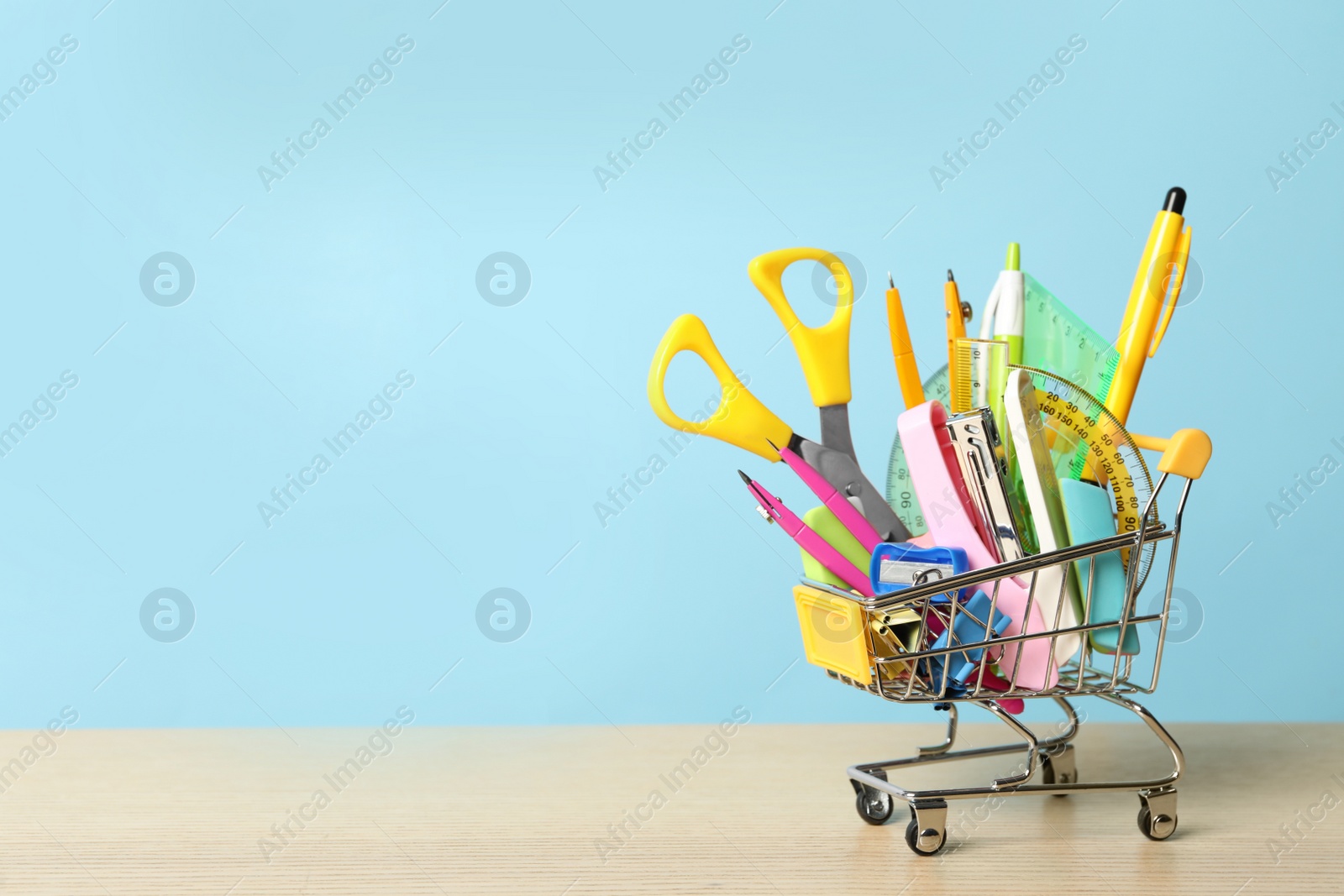 Photo of Small cart with different school stationery on wooden table against light blue background, space for text. Back to school