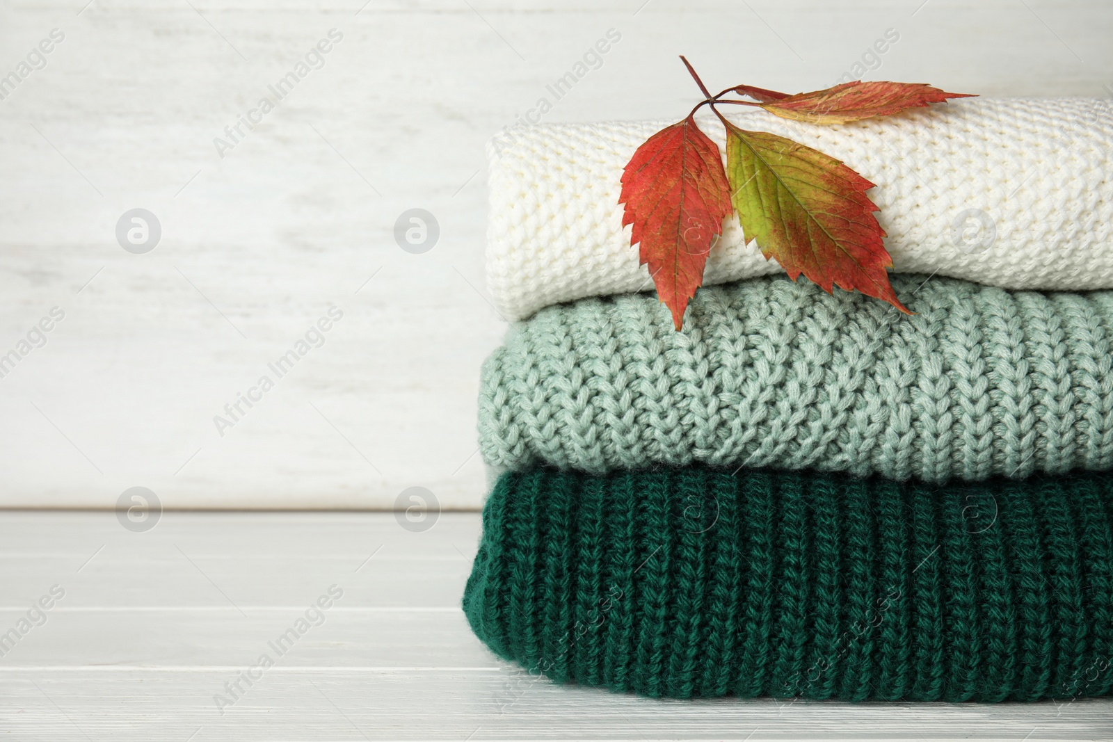 Photo of Stack of knitted clothes on white wooden background, space for text. Cozy autumn