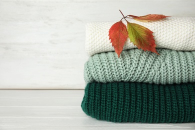 Photo of Stack of knitted clothes on white wooden background, space for text. Cozy autumn