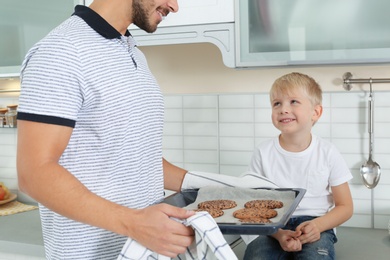 Young man treating his son with homemade oven baked cookies in kitchen