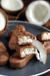 Photo of Delicious milk chocolate candy bars with coconut filling on grey plate, closeup