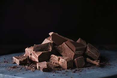 Pieces of tasty dark chocolate on grey board against black background