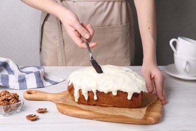 Photo of Woman spreading cream onto sweet cake at white wooden table, closeup
