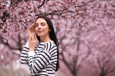 Photo of Pretty young woman near blooming tree in park, space for text. Spring look