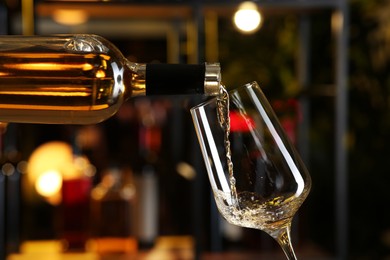 Pouring white wine from bottle into glass on blurred background, closeup