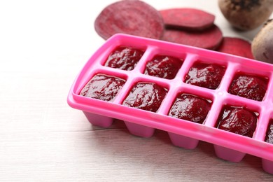 Photo of Beet puree in ice cube tray on white wooden table, closeup. Ready for freezing