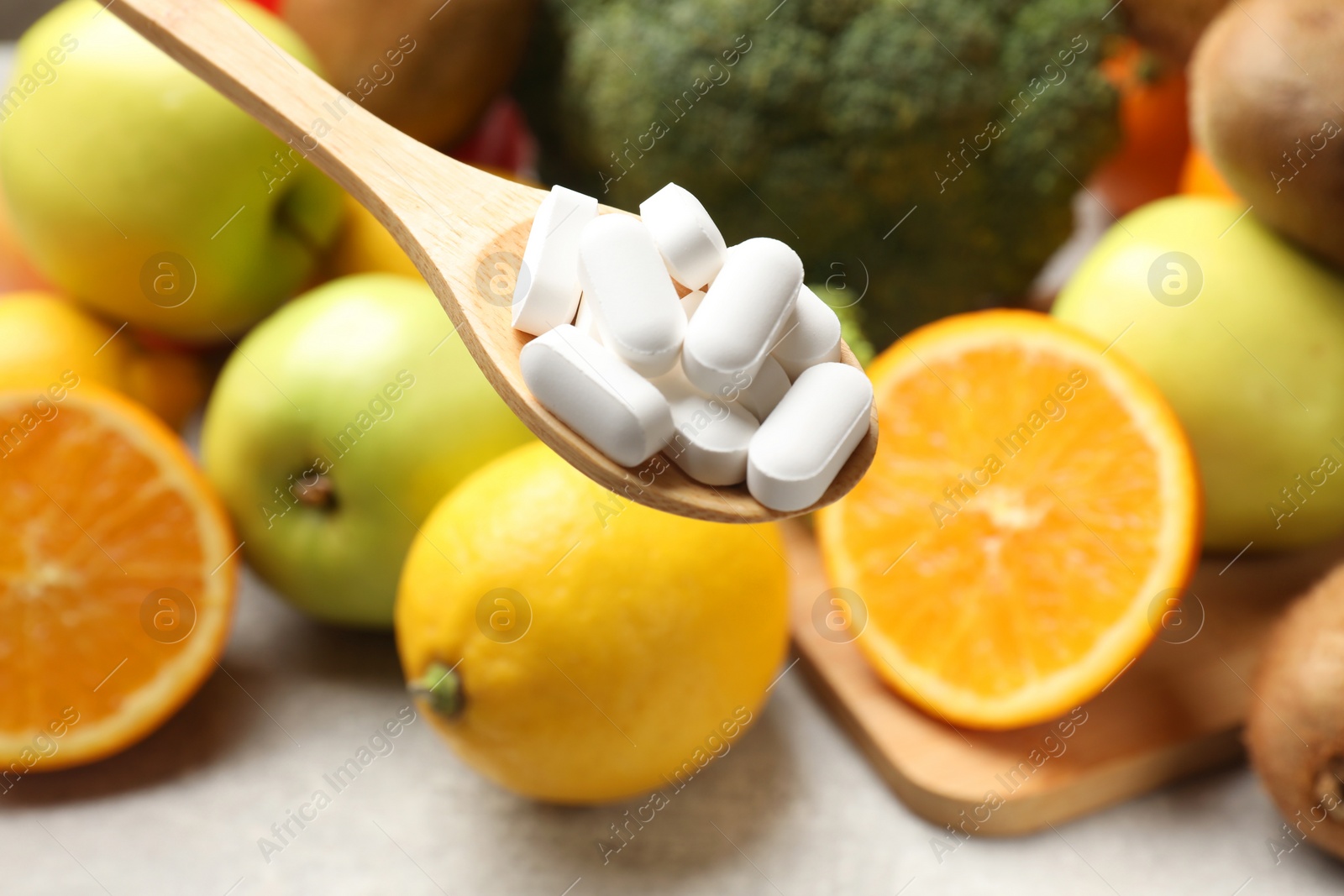 Photo of Dietary supplements. Spoon with pills over food products at grey table, closeup