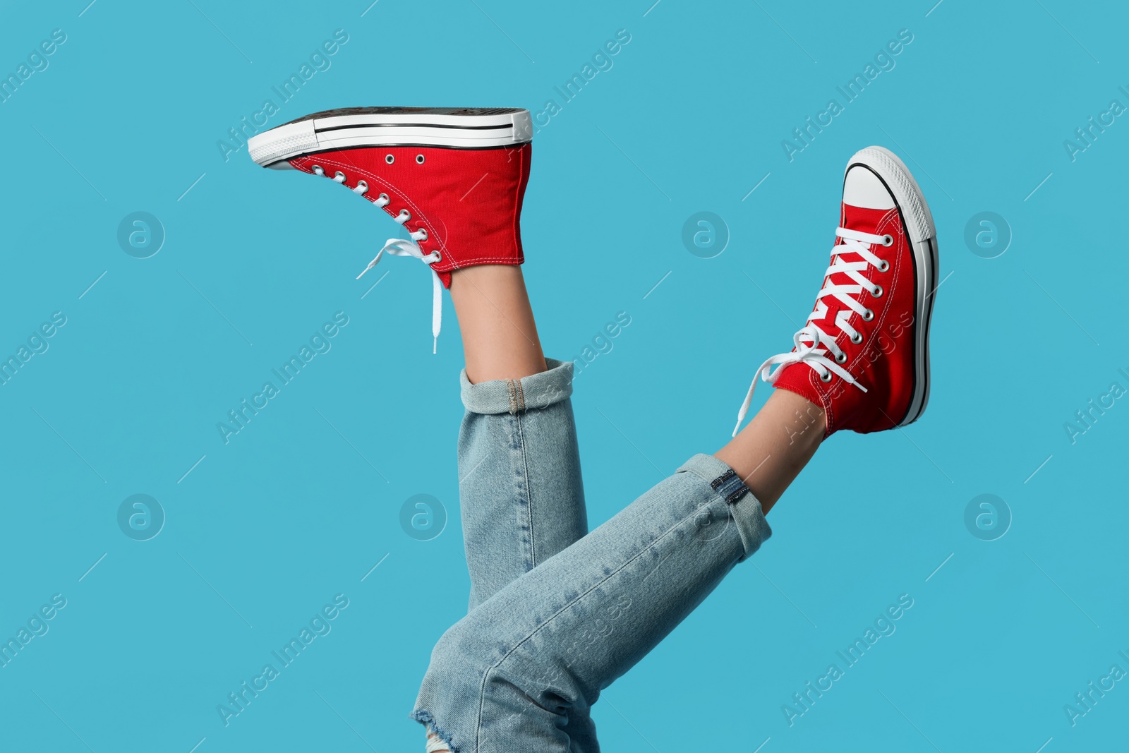 Photo of Woman in stylish gumshoes on light blue background, closeup