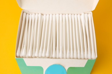 Photo of Cardboard box with new cotton buds on yellow background, closeup