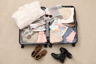 Photo of Open suitcase with warm clothes, accessories and shoes on floor, flat lay