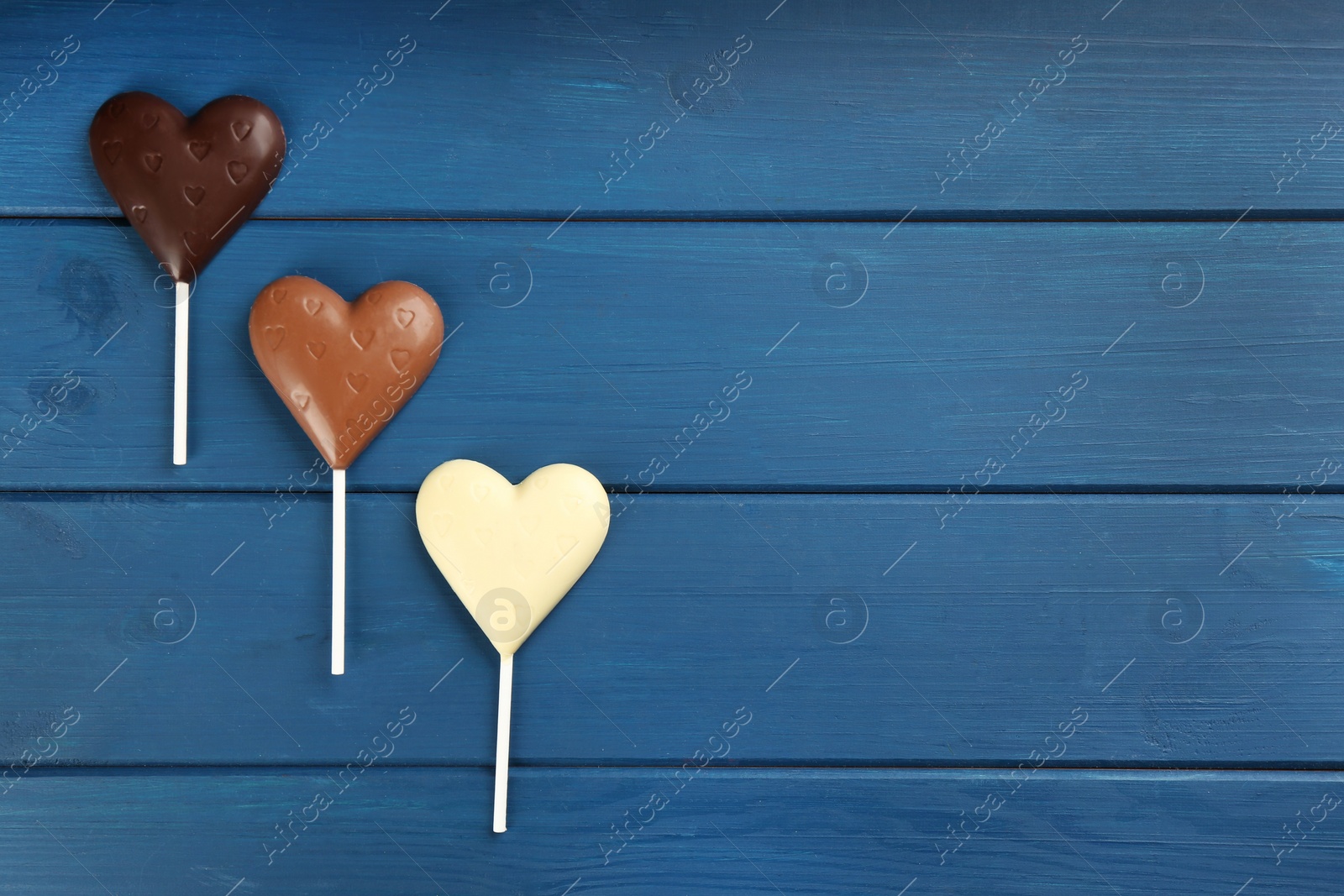Photo of Different chocolate heart shaped lollipops on blue wooden table, flat lay. Space for text