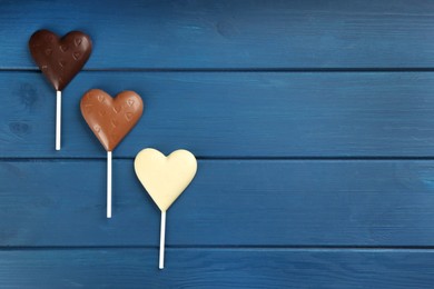 Photo of Different chocolate heart shaped lollipops on blue wooden table, flat lay. Space for text