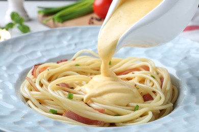 Photo of Pouring tasty cheese sauce onto spaghetti with meat, closeup