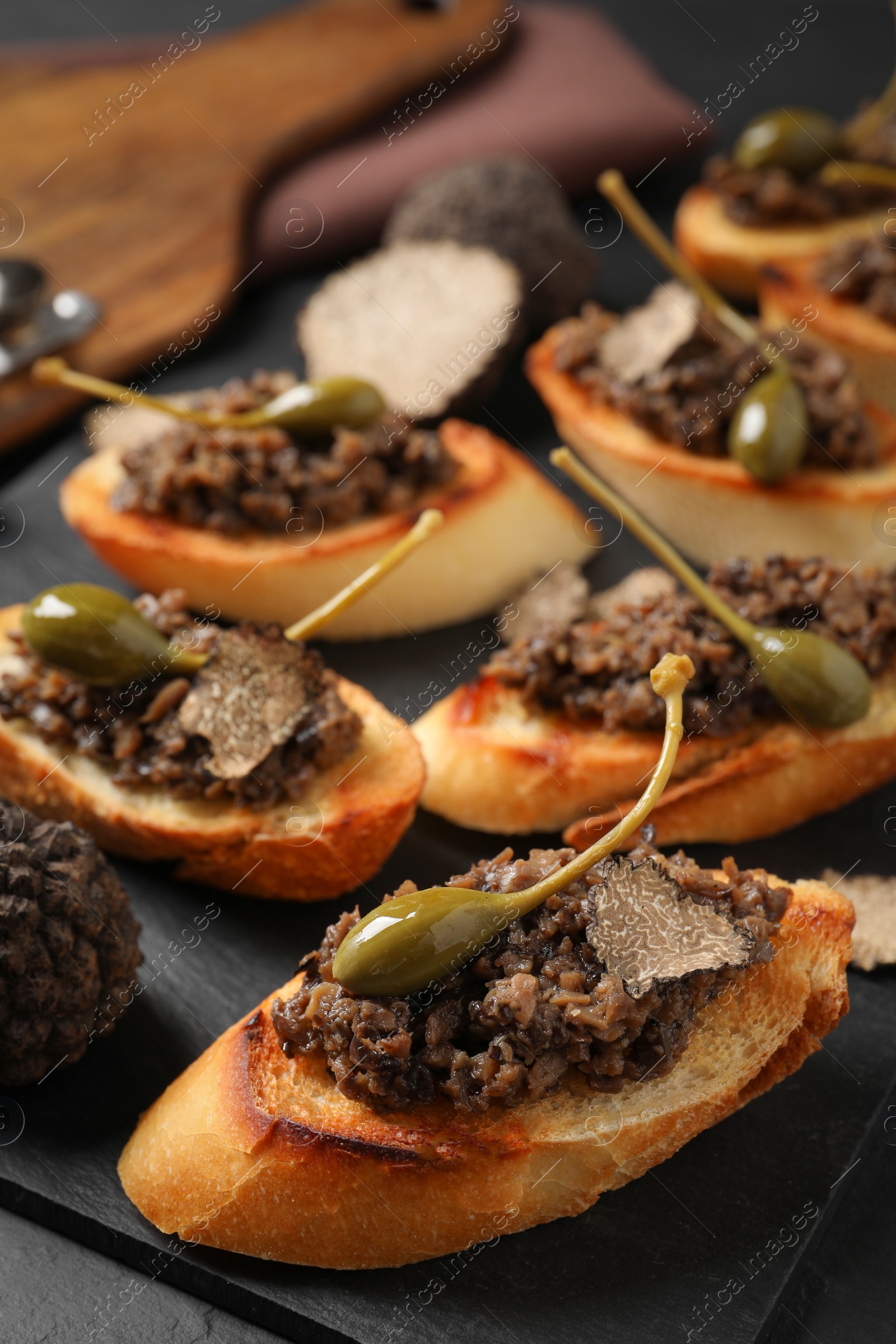 Photo of Tasty bruschettas with truffle paste and capers on black table, closeup