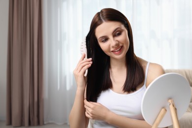Beautiful woman brushing her hair near mirror in room, space for text