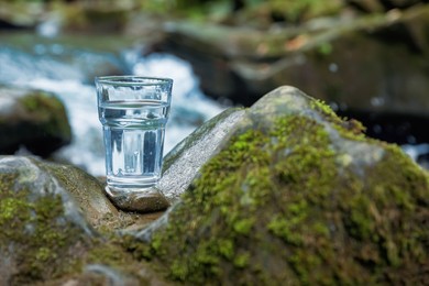 Glass of fresh water on stone with moss near stream. Space for text