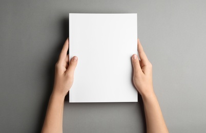 Woman holding brochure with blank cover on grey background, top view. Mock up for design