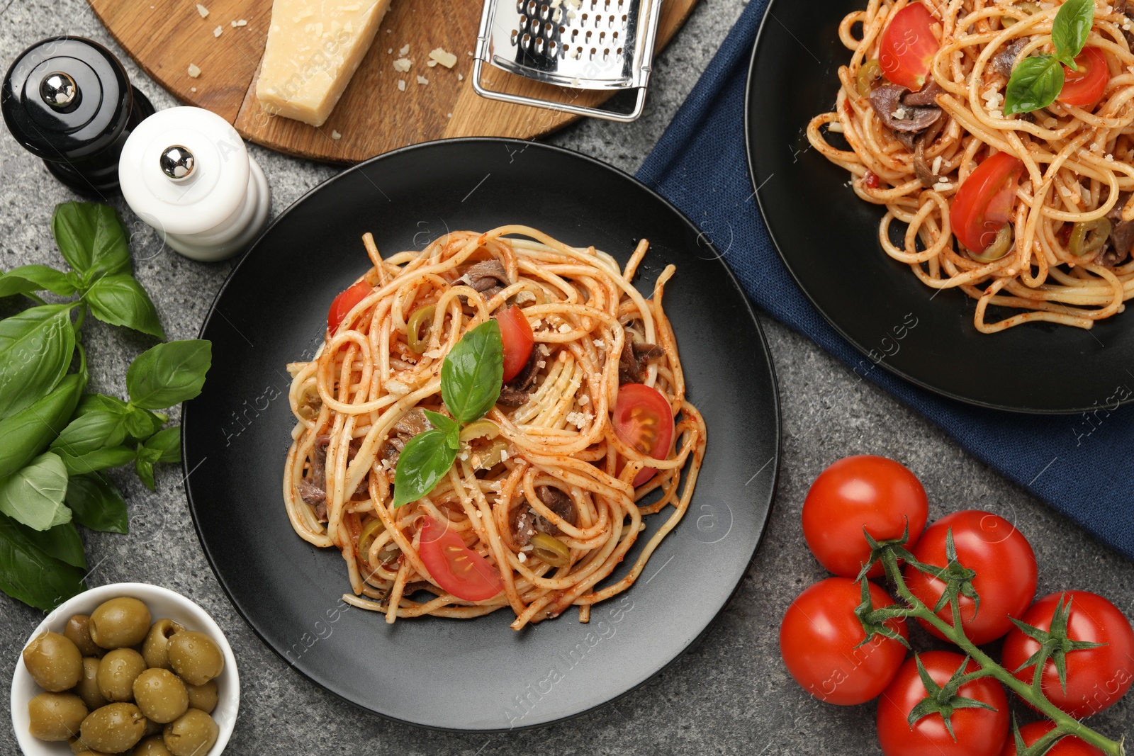 Photo of Delicious pasta with anchovies, tomatoes and olives on grey table, flat lay