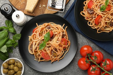 Photo of Delicious pasta with anchovies, tomatoes and olives on grey table, flat lay