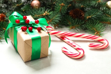 Christmas gift box with green bow, candy canes and festive decor on light table. Space for text