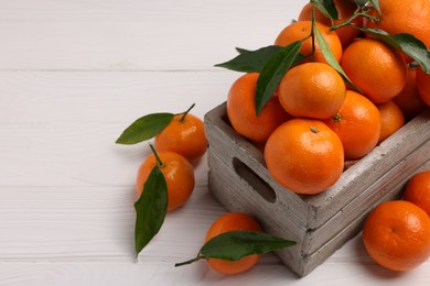 Photo of Delicious tangerines with leaves in crate on white wooden table, closeup. Space for text