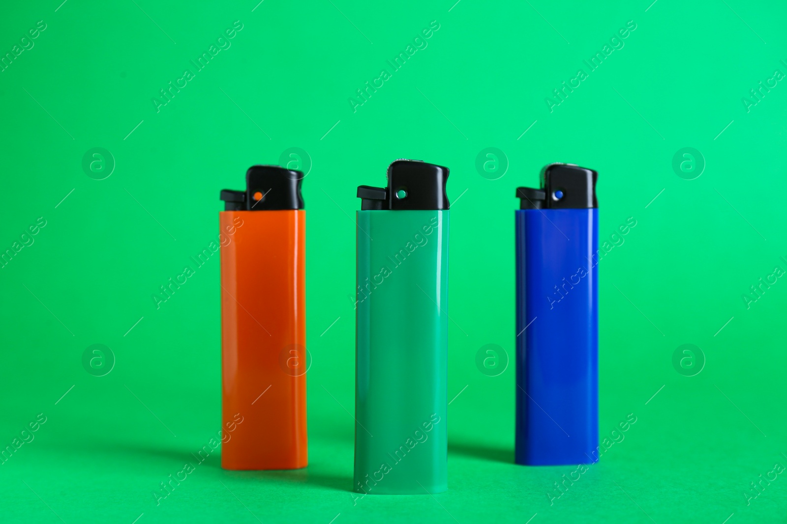 Photo of Stylish small pocket lighters on green background