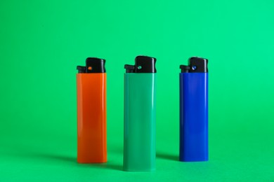 Stylish small pocket lighters on green background