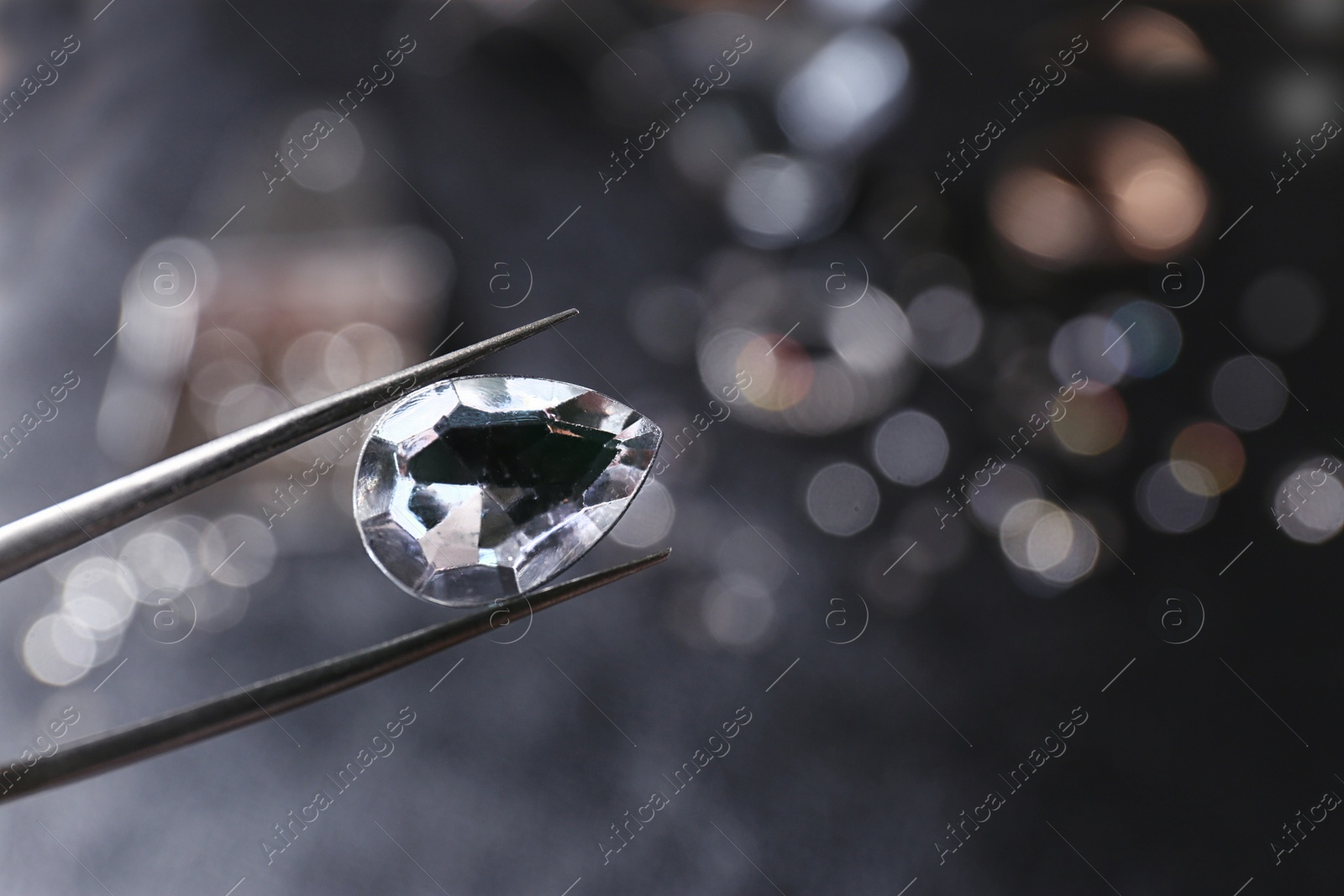 Photo of Tweezers with jewel over table. Space for text