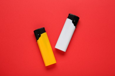Photo of Stylish small pocket lighters on red background, flat lay