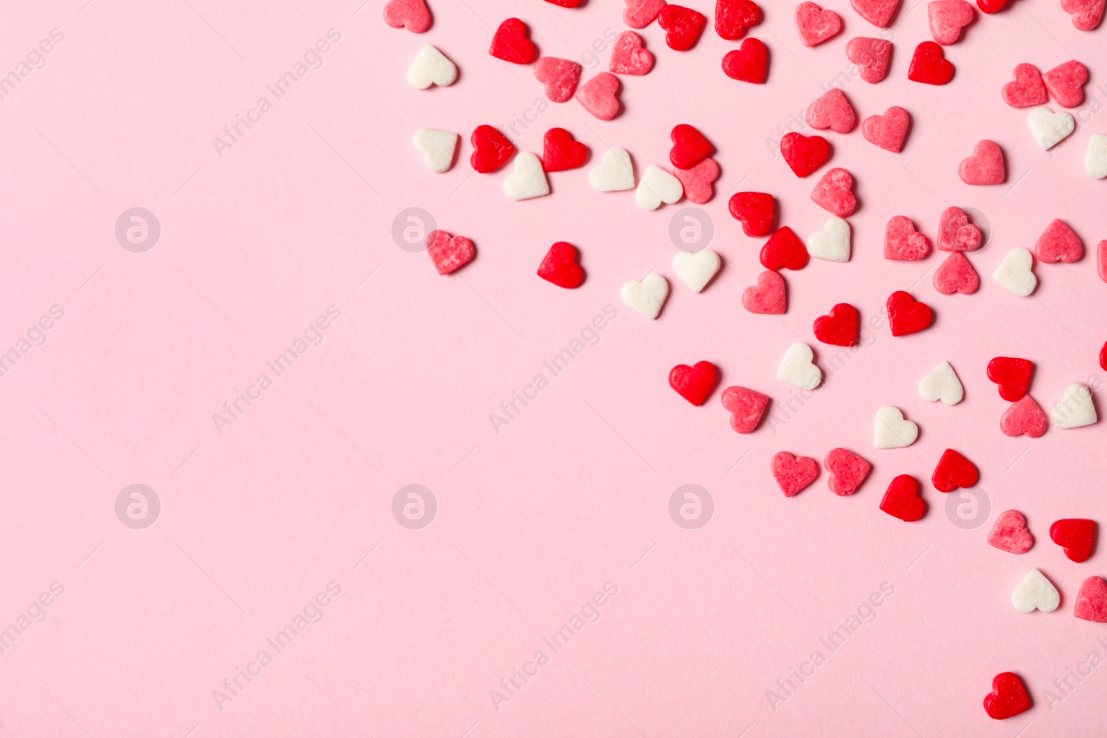 Photo of Heart shaped sprinkles on pink background, flat lay. Space for text