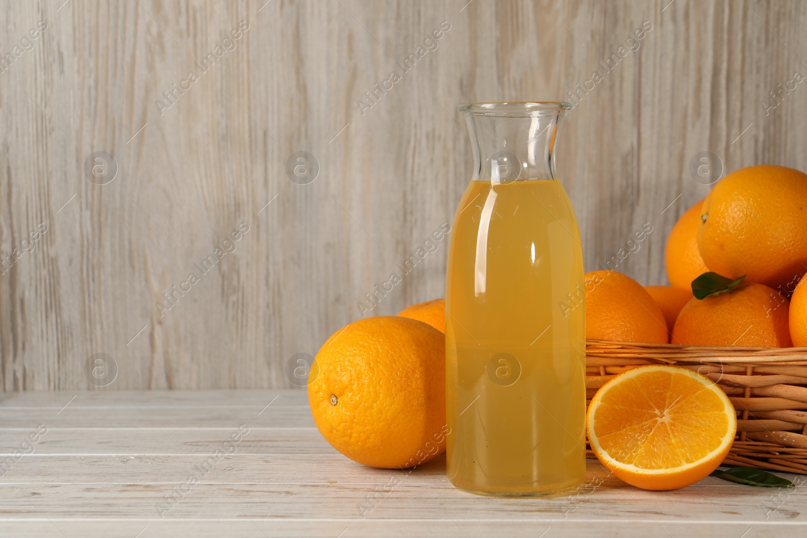 Photo of Many ripe oranges and fresh juice on light wooden table, space for text