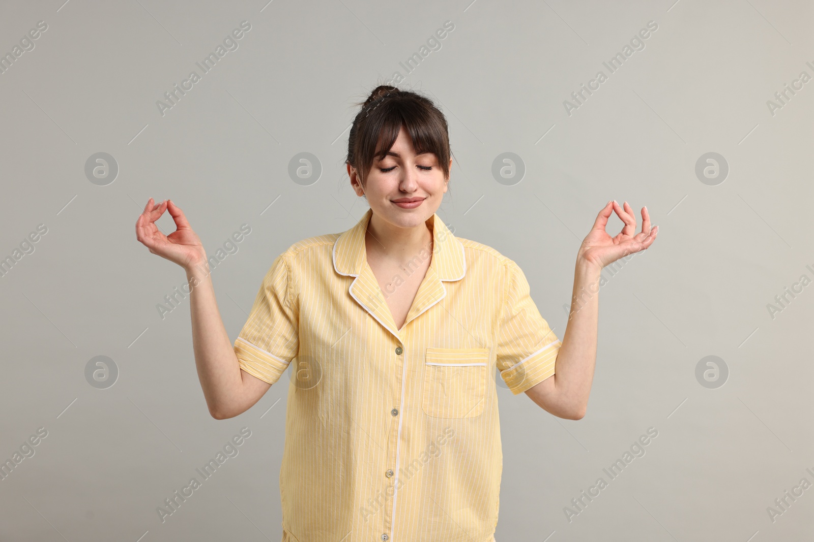 Photo of Woman in pyjama meditating on grey background